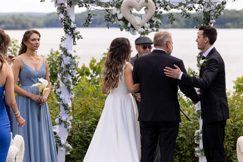 Brittany and Cole's wedding ceremony on Stout’s Island, Wisconsin, with decorated arbor and lake backdrop.