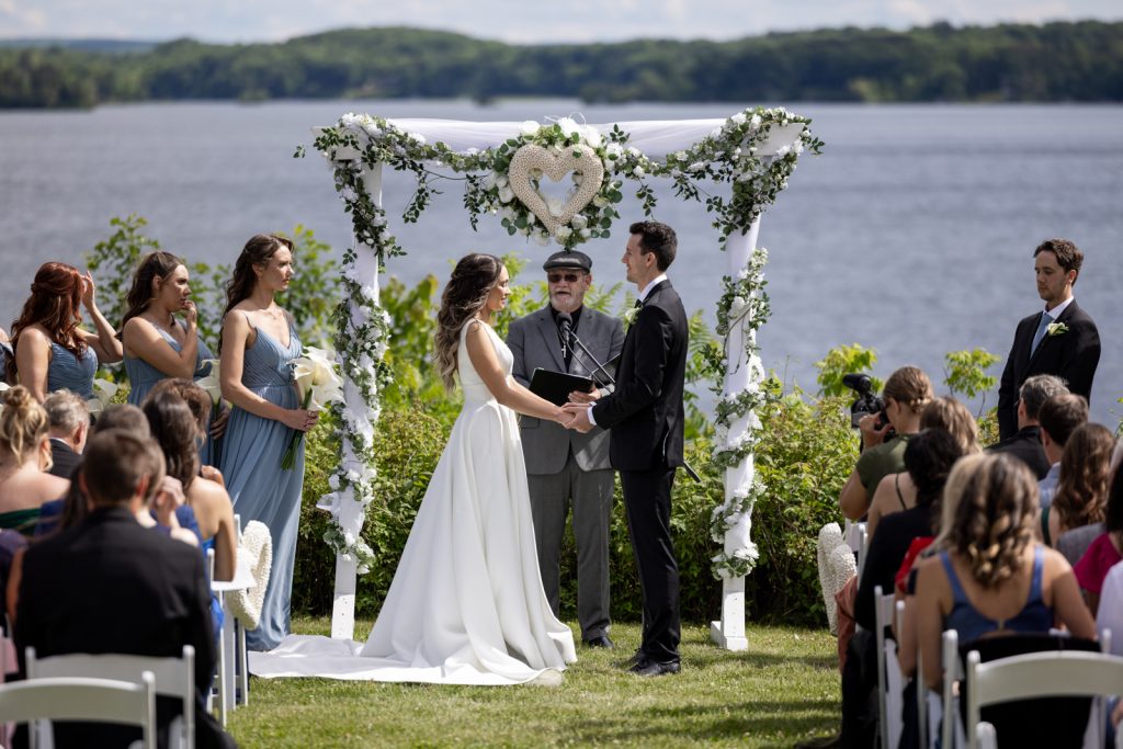Brittany and Cole wedding ceremony on Stout’s Island, Wisconsin, with floral arch and lake backdrop.