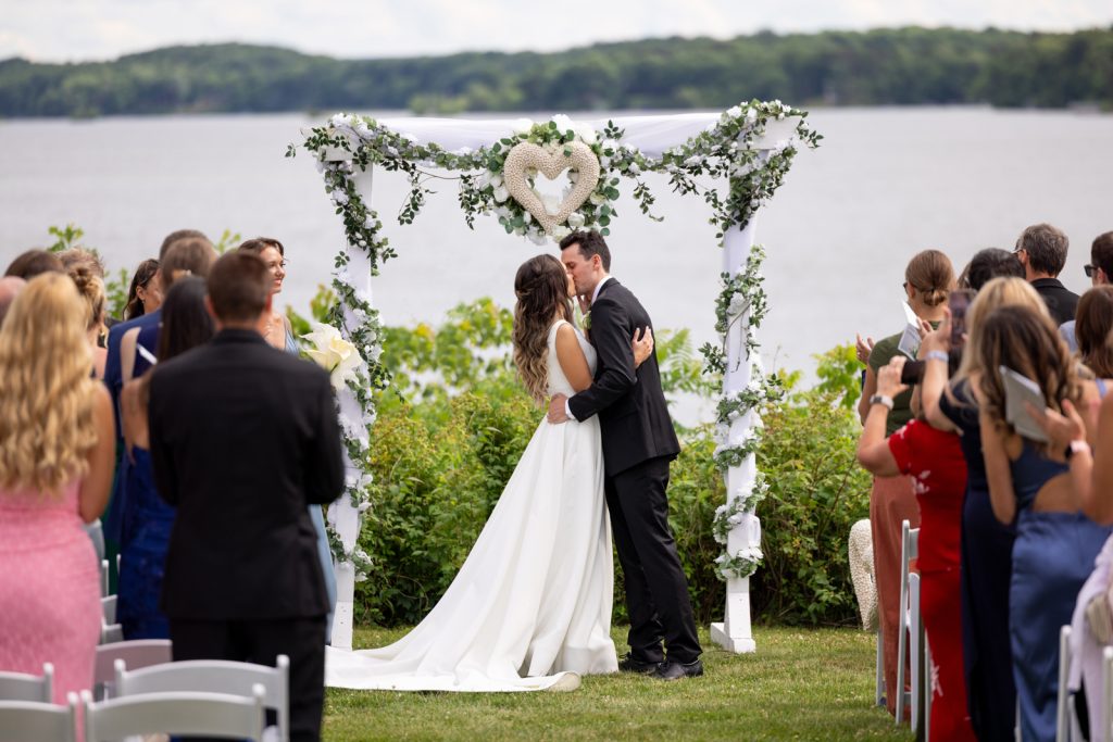 Bride and groom kissing at Stout’s Island wedding ceremony overlooking Red Cedar Lake.