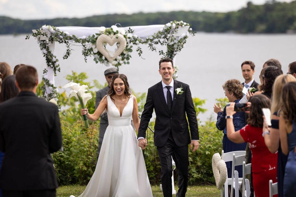 Brittany and Cole walking through Stout’s Island wedding ceremony, lakeside view and floral arch.