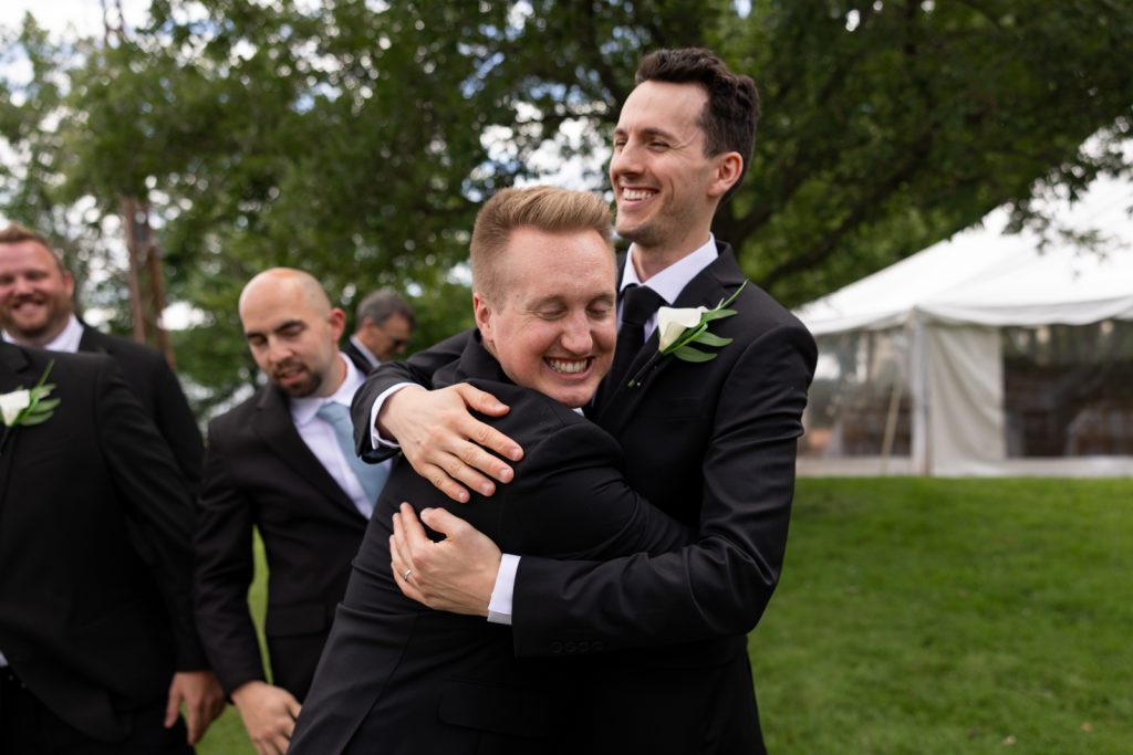 Brittany and Cole's Stout’s Island wedding: groomsmen embracing, joyful celebration on Red Cedar Lake.