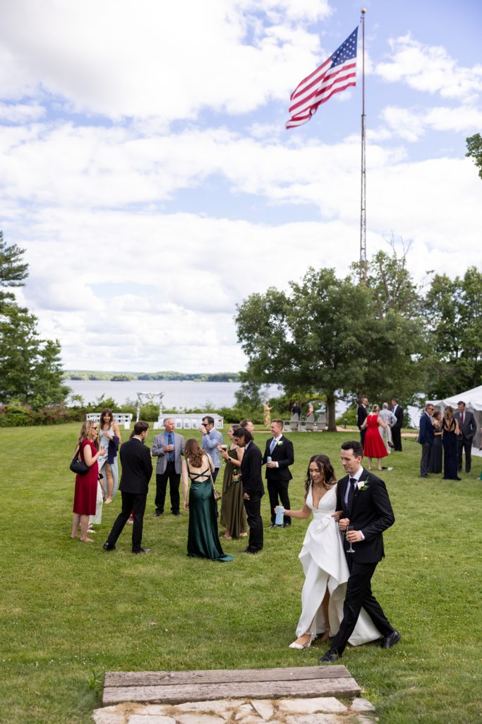 Brittany and Cole walking at Stout’s Island wedding reception, American flag waving in background, Red