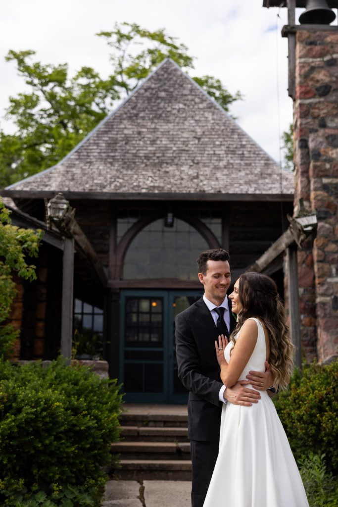 Brittany and Cole embracing in front of Stout’s Island Lodge boat house, Wisconsin wedding photography.
