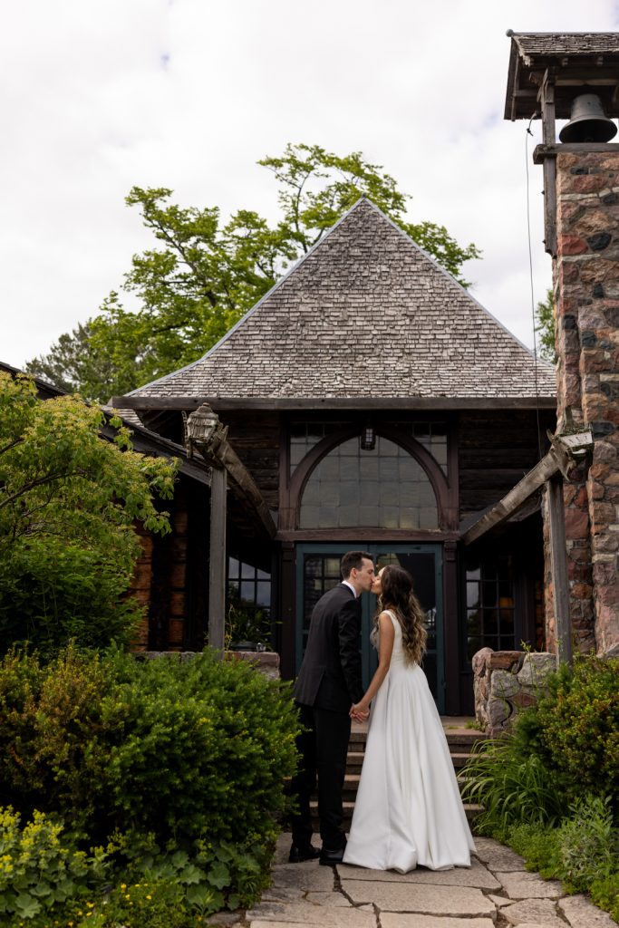 Brittany and Cole kissing in front of Stout’s Island Lodge boat house, Wisconsin wedding photography.