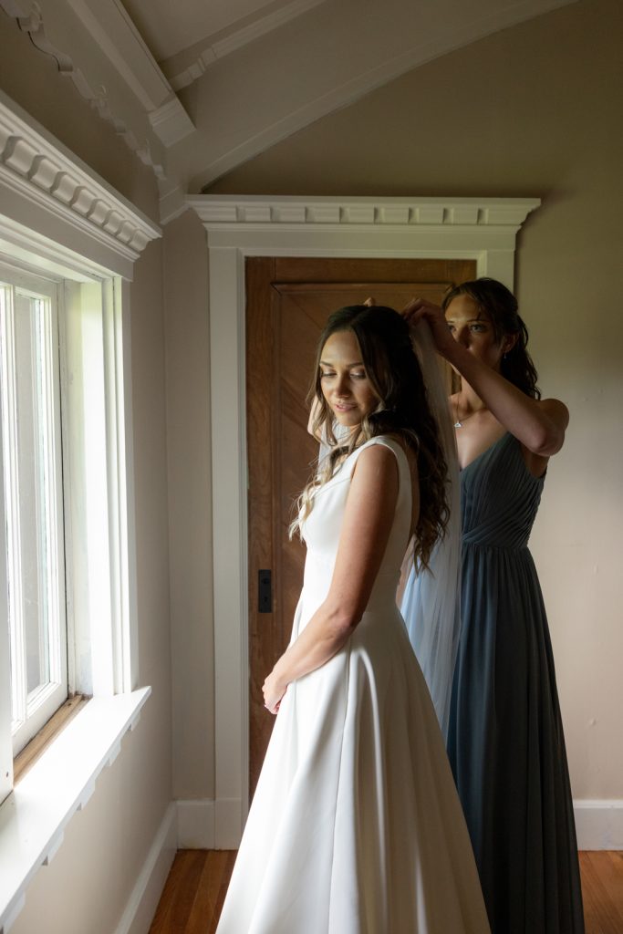 Bride in wedding dress with bridesmaid adjusting hair, Stout’s Island wedding preparation.