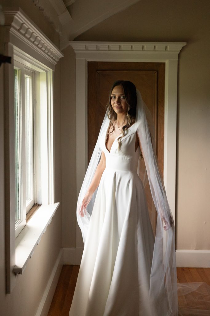 Bride in wedding gown and veil near window at Stout’s Island Lodge.