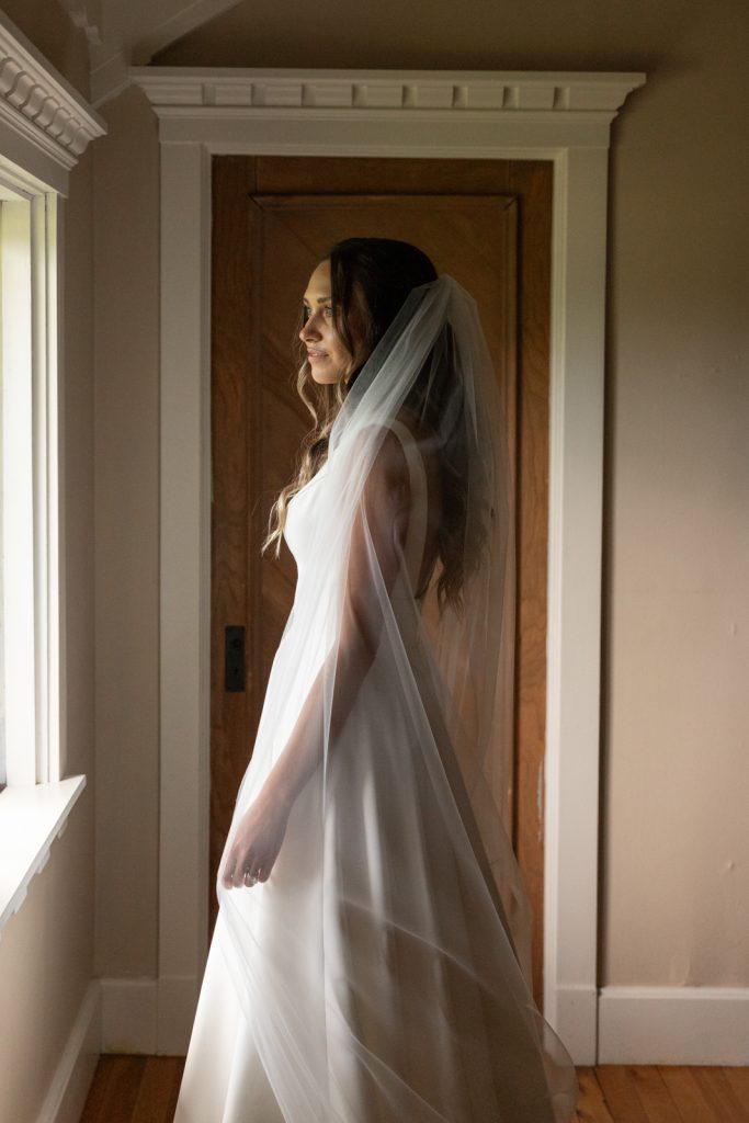 Bride in wedding dress and veil near window at Stout’s Island wedding venue