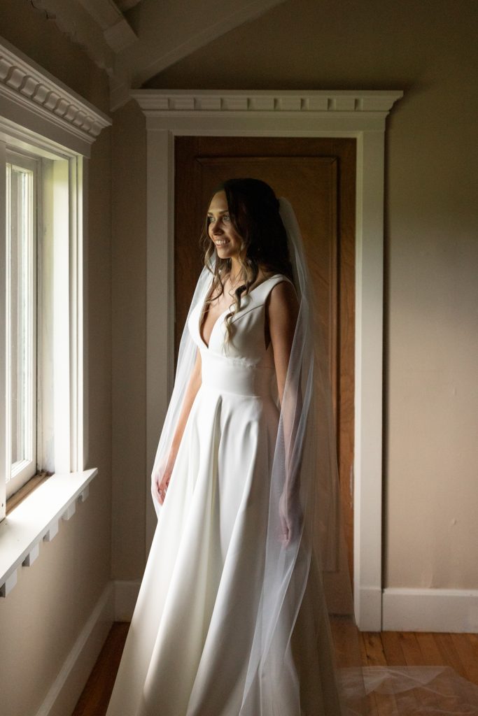 Bride in wedding dress and veil near window at Stout’s Island Lodge.