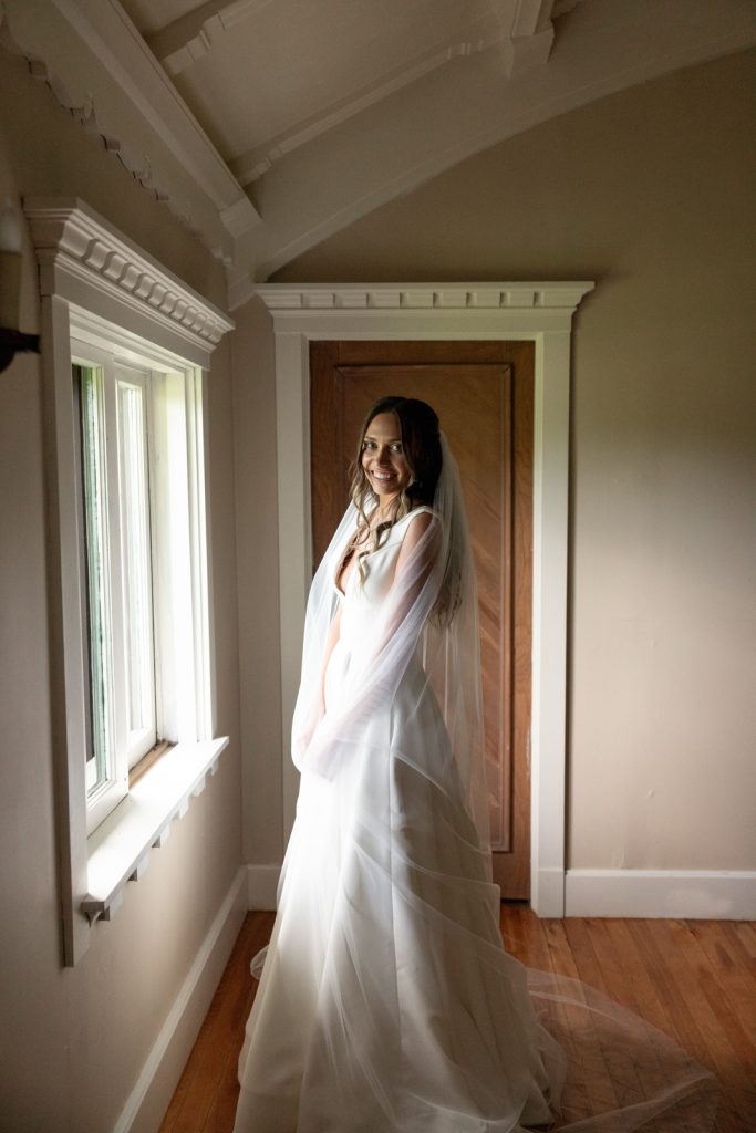 Bride in wedding dress and veil near window at Stout’s Island Lodge.