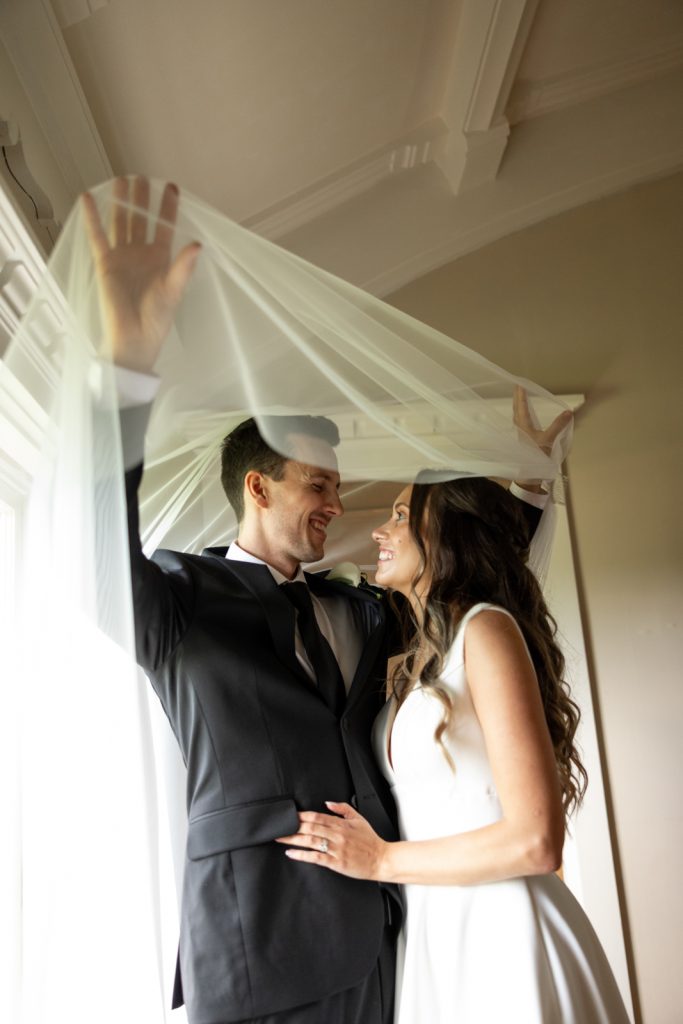 Brittany and Cole, Stout’s Island wedding couple, bride and groom under a veil, joyful moment