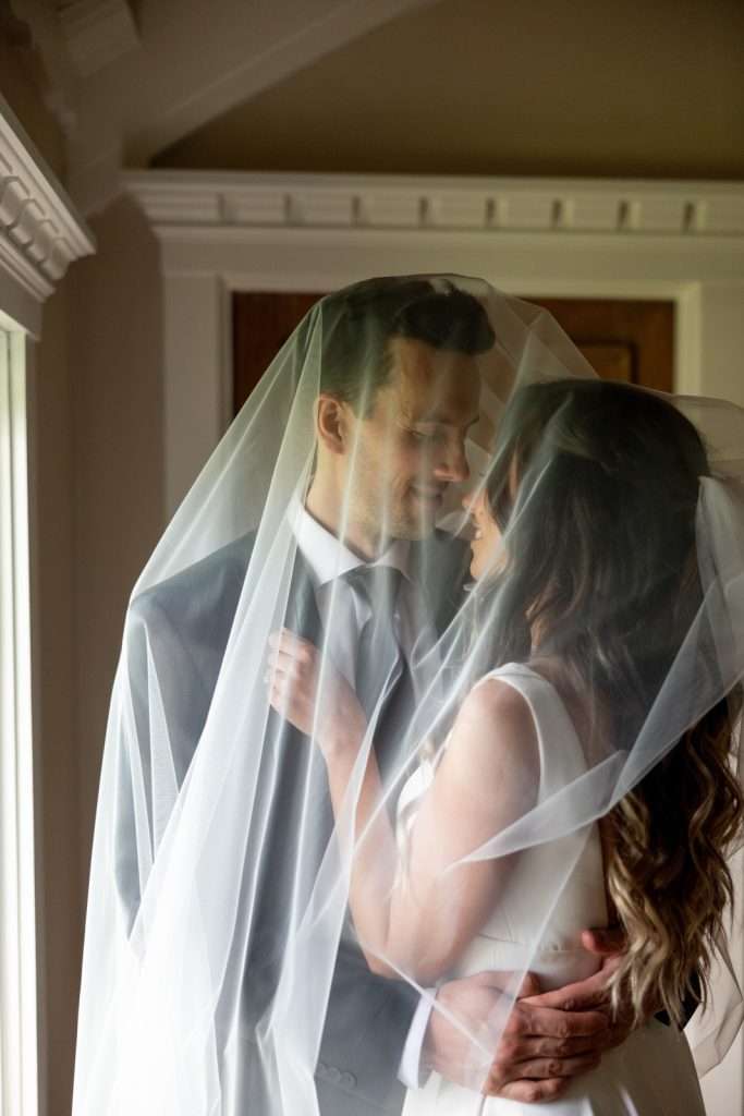 Brittany and Cole embracing under a wedding veil at Stout’s Island Lodge, Wisconsin.