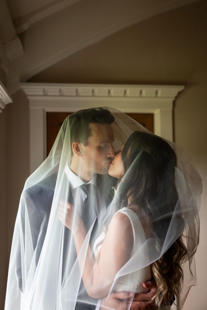 Brittany and Cole sharing a kiss under a veil at their Stout’s Island wedding in