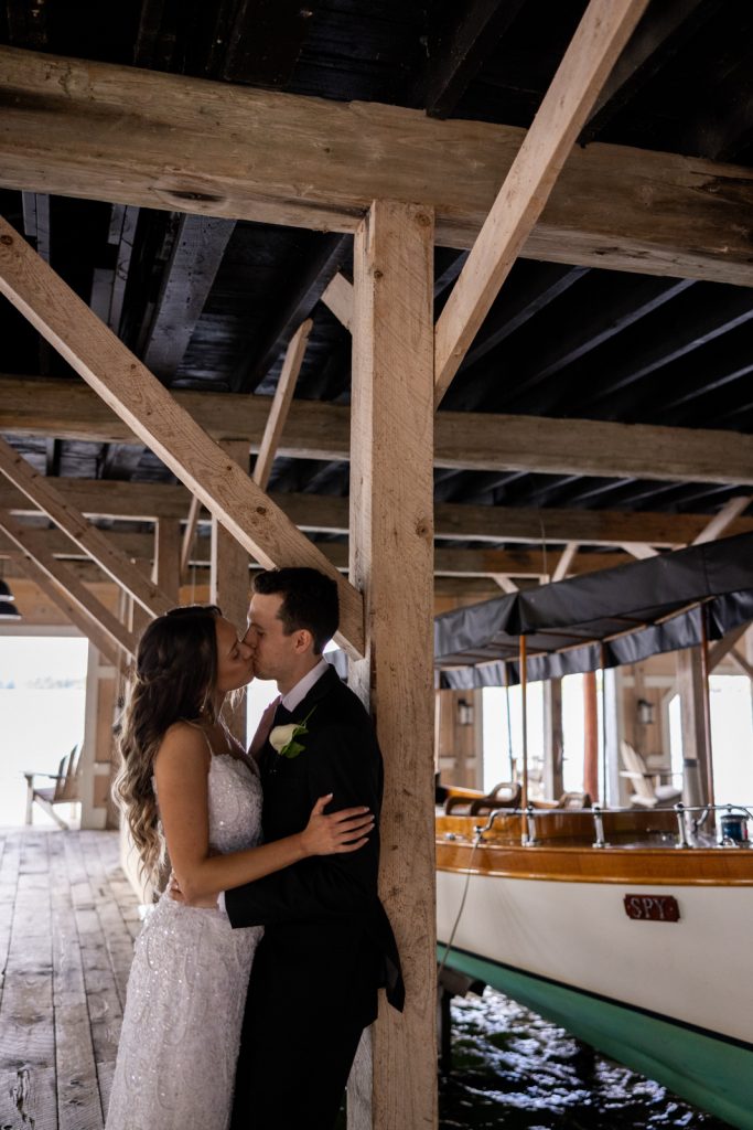 Brittany and Cole kissing under the boat house at Stout’s Island wedding venue in Birchwood,
