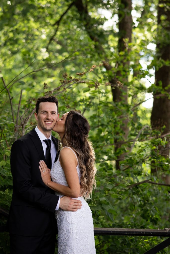 Brittany and Cole sharing a kiss amidst lush greenery at Stout’s Island wedding in Wisconsin.
