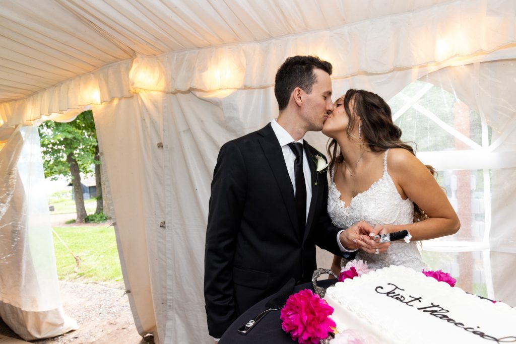 Brittany and Cole kissing and cutting wedding cake at Stout’s Island Lodge in Wisconsin