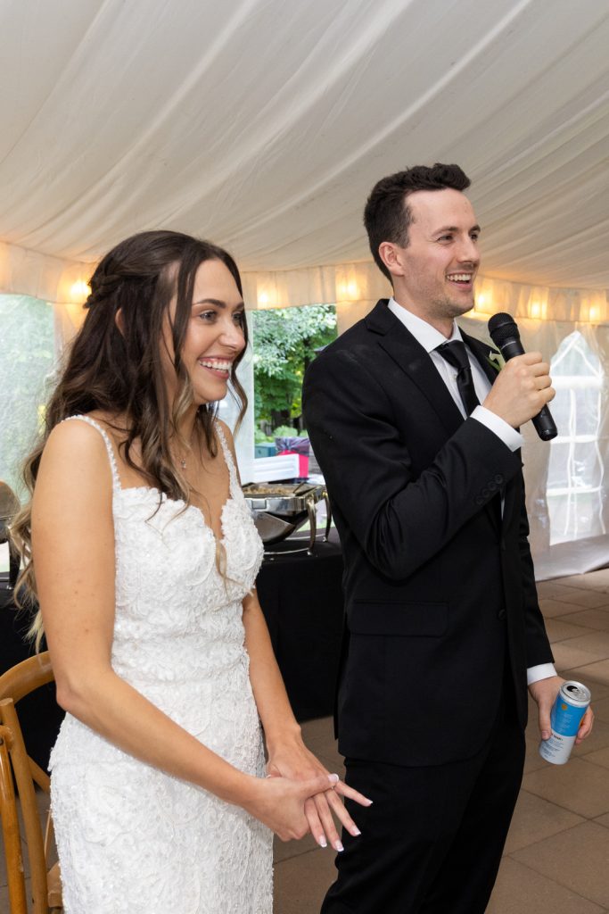 Brittany and Cole at their Stout’s Island wedding reception, groom speaking into microphone.