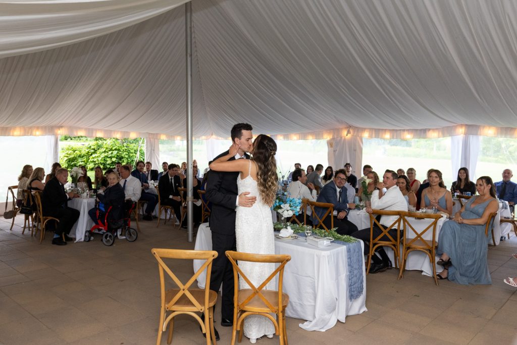 Brittany and Cole kissing at their Stout’s Island wedding reception under a white tent.
