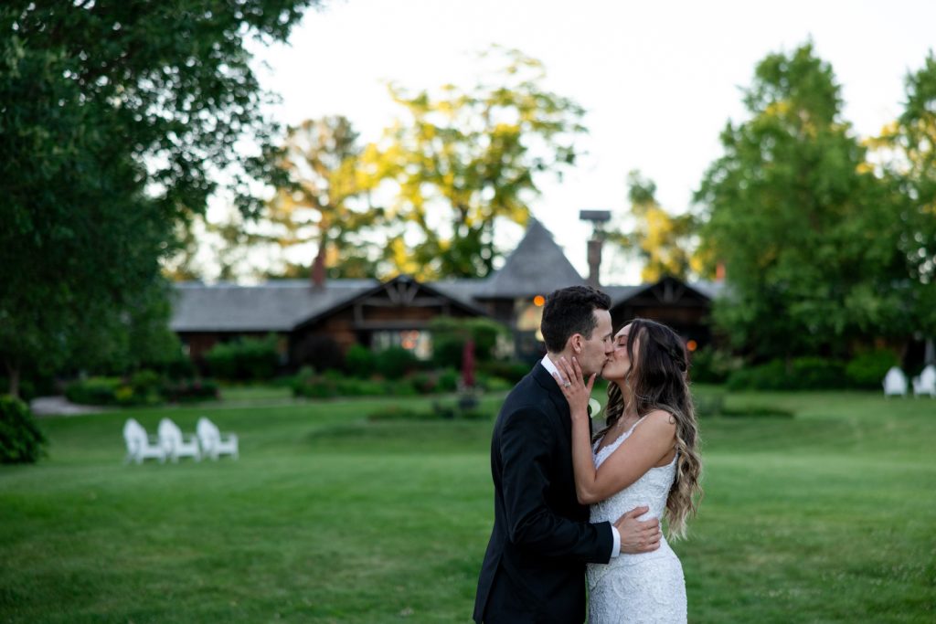 Brittany and Cole kissing at Stout’s Island wedding in Birchwood, Wisconsin, with resort lodge in