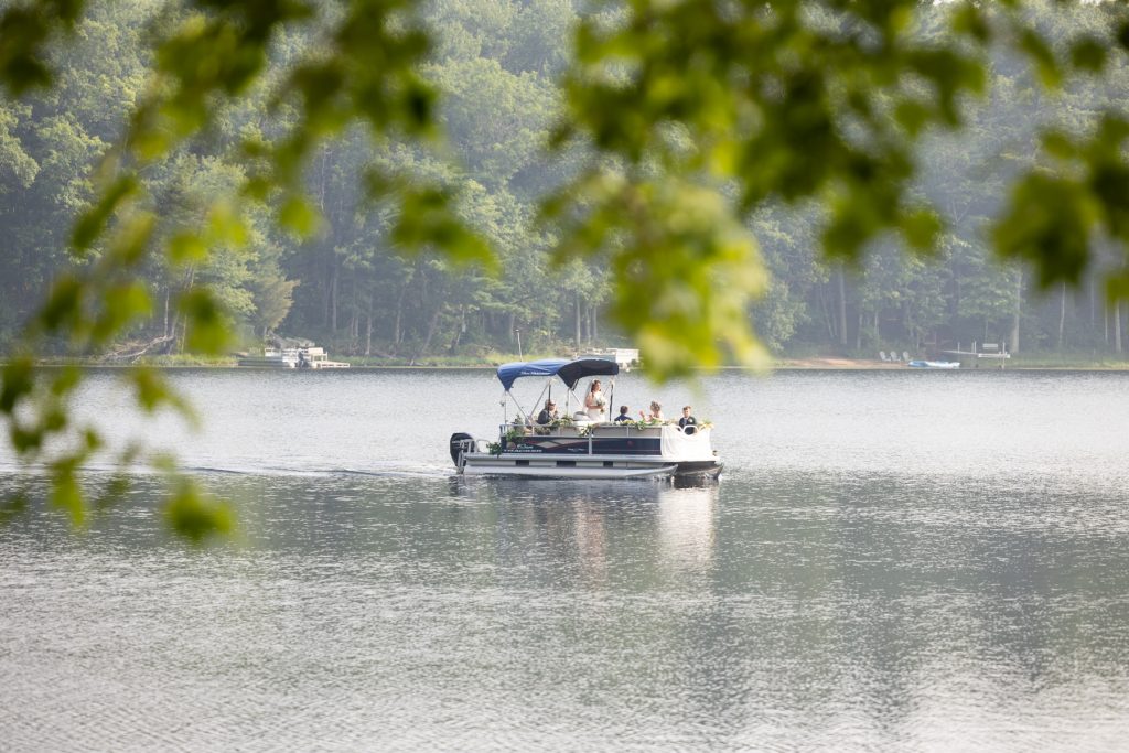 Bride arriving by pontoon boat at lake-side wedding in Hayward, WI