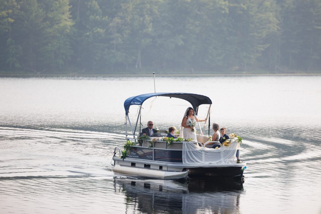 Bride arriving by pontoon boat at lake-side wedding in Hayward, WI