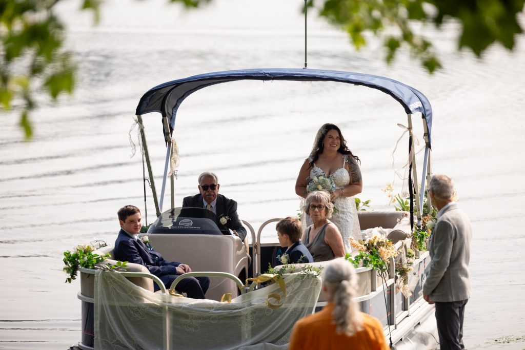 Bride arriving by pontoon boat at a lake wedding in Hayward, WI.