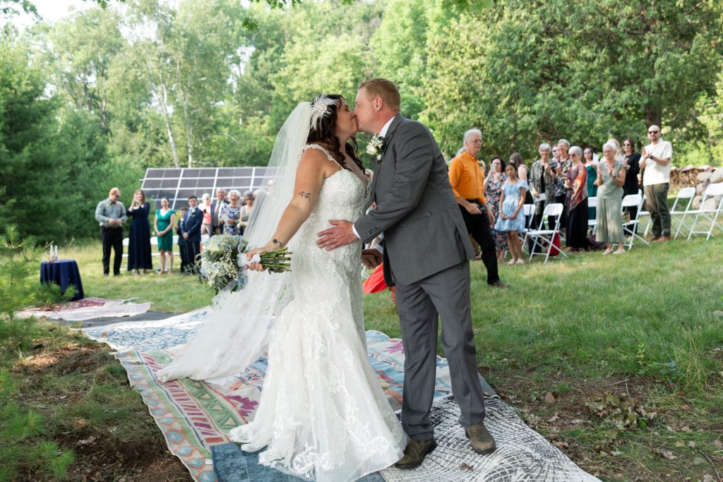 Bride and groom kissing at lakeside wedding in Hayward, WI, surrounded by guests