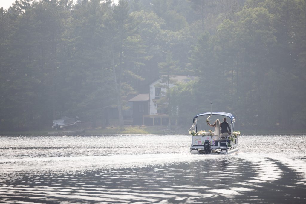 Bride arriving by pontoon boat at lake-side wedding ceremony in Hayward, WI