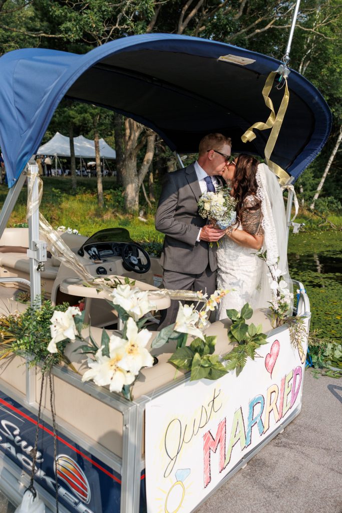 Bride and groom kissing on pontoon boat decorated with flowers and "Just Married" sign, Hayward,