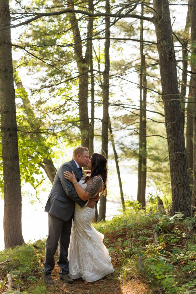 Bride and groom kissing in wooded lakeside setting at Hayward, WI wedding.