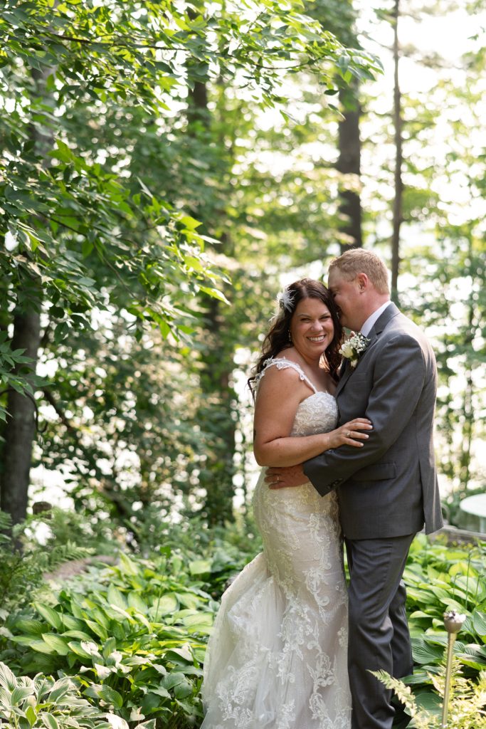 Bride and groom embracing in wooded lakeside setting at Hayward, WI wedding.