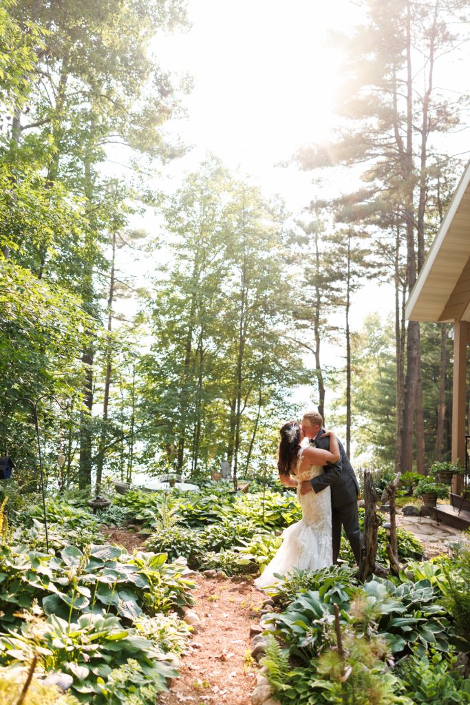 Bride and groom kissing in backyard wedding setting overlooking lake in Hayward, WI