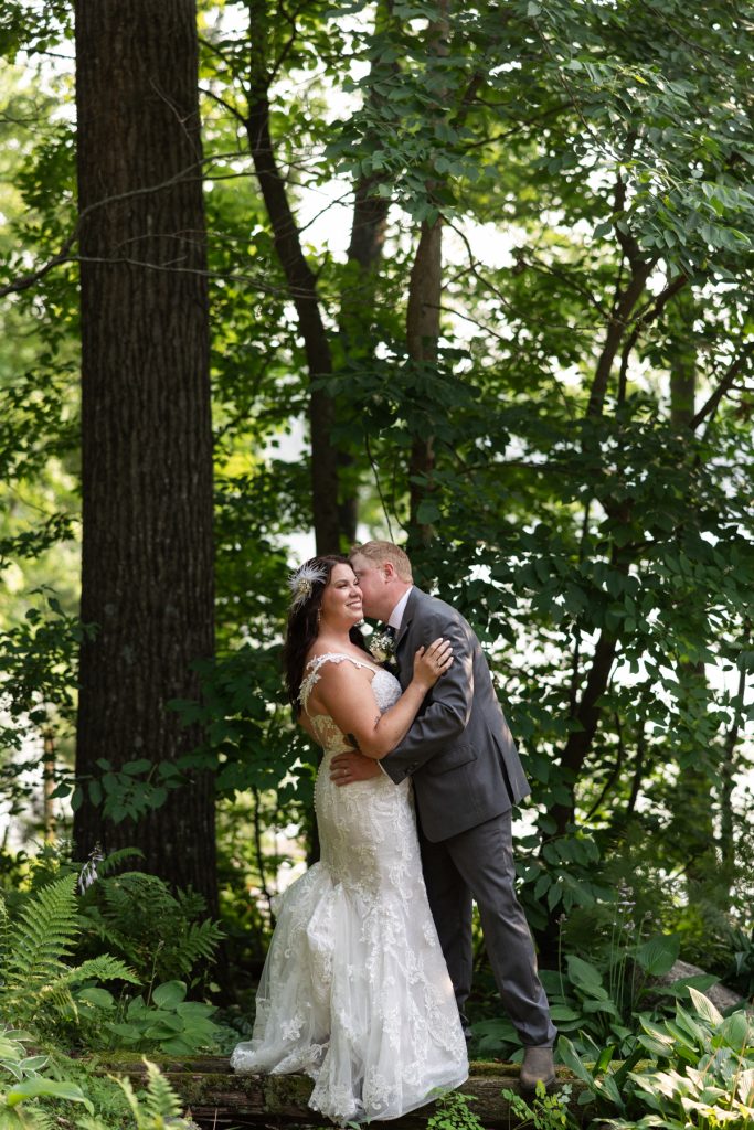 Bride and groom embracing in wooded lakeside setting at Hayward, WI wedding.