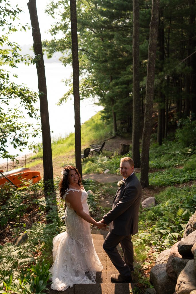 Bride and groom holding hands on lakeside steps at Hayward, WI wedding.