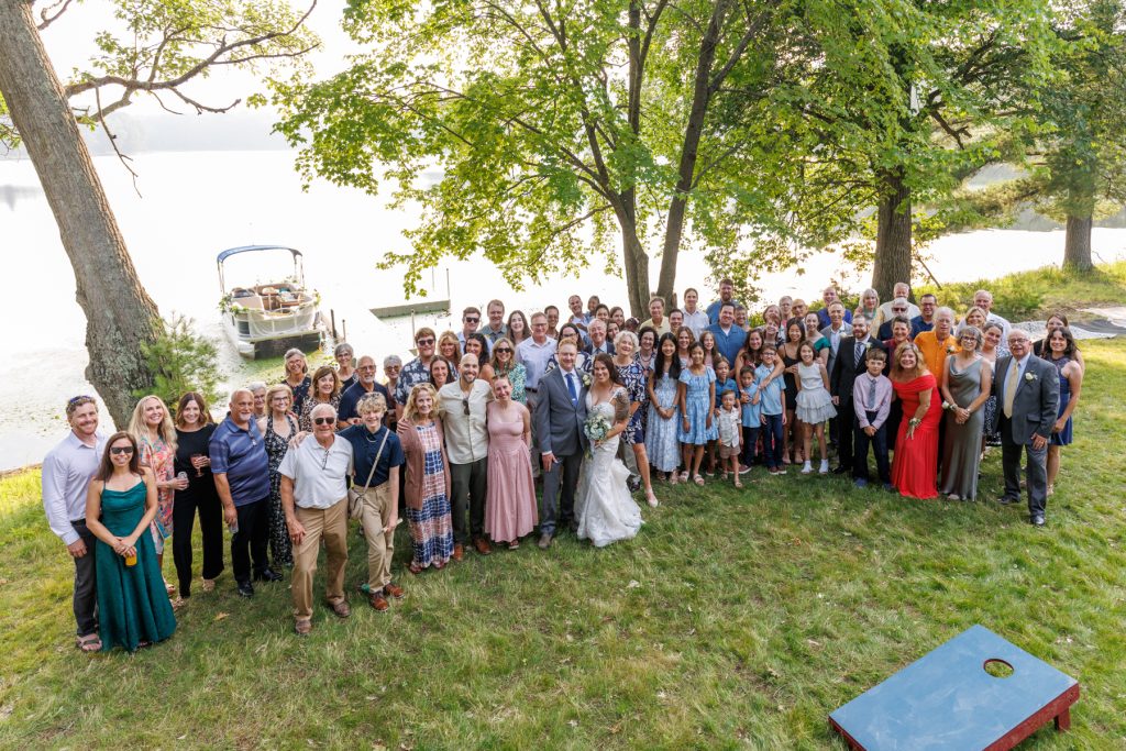 Large group wedding photo at lakefront cabin in Hayward, WI, bride and groom in foreground