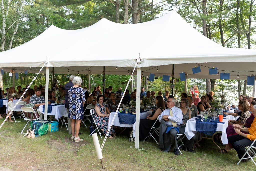 Wedding reception at family cabin in Hayward, WI, with guests seated under a tent.