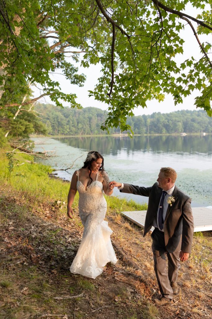 Bride and groom walking hand-in-hand near lake at Hayward, WI wedding.
