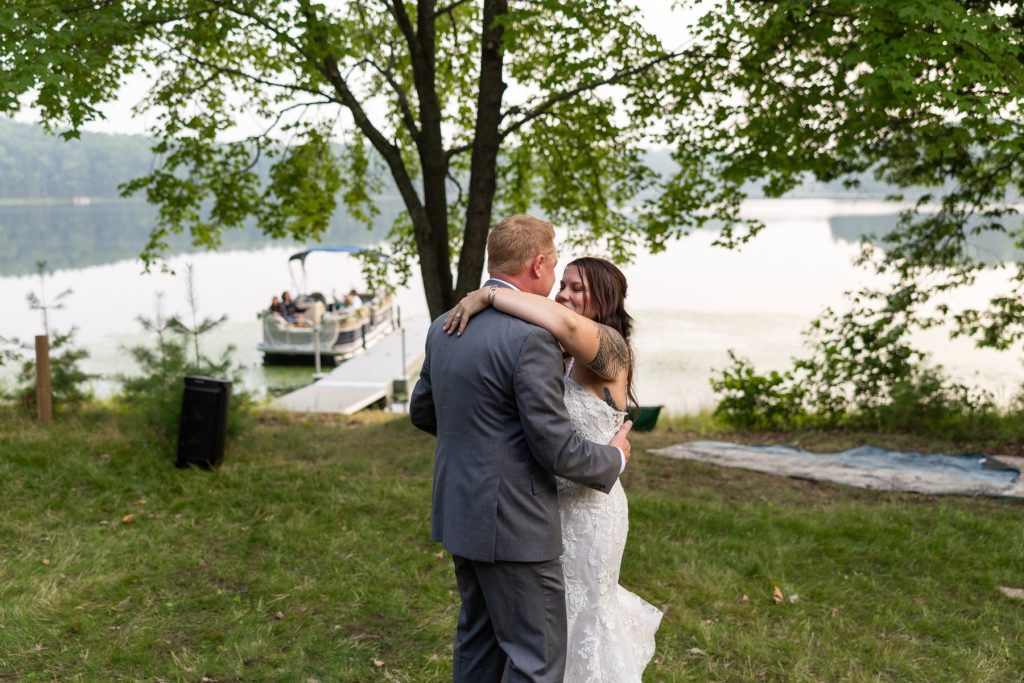 Bride and groom embracing near lake and pontoon boat at Hayward, WI wedding