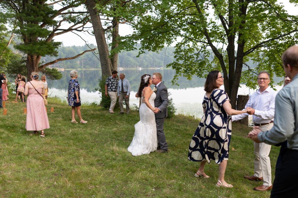 Bride and groom kissing at a lakeside wedding in Hayward, WI, surrounded by family and