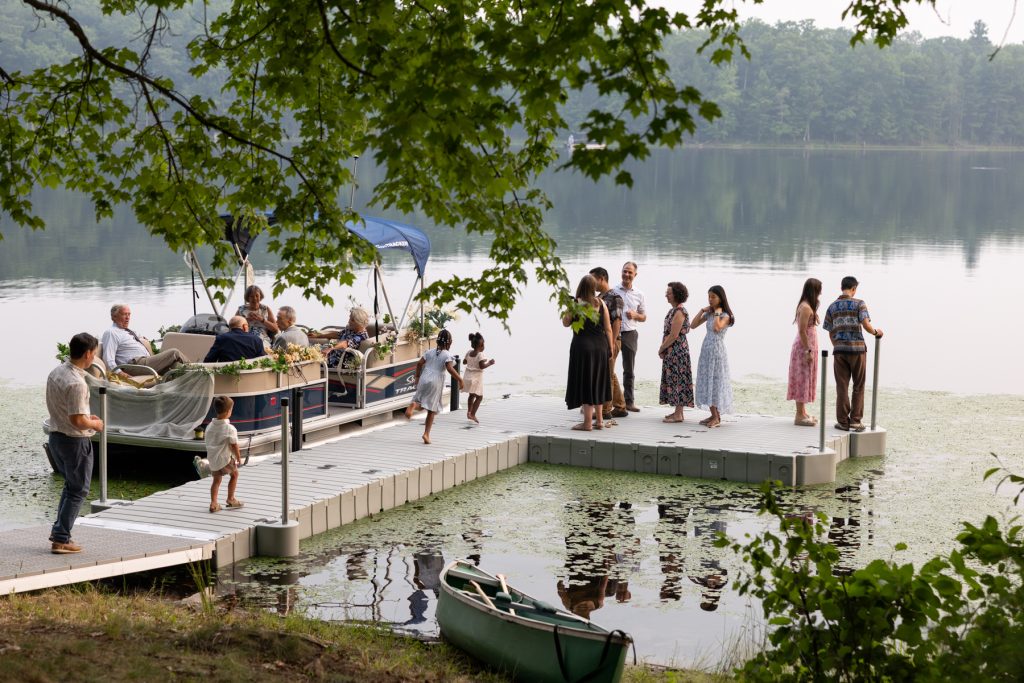 Bride and groom on dock with guests and pontoon boat at Hayward, WI lake wedding.