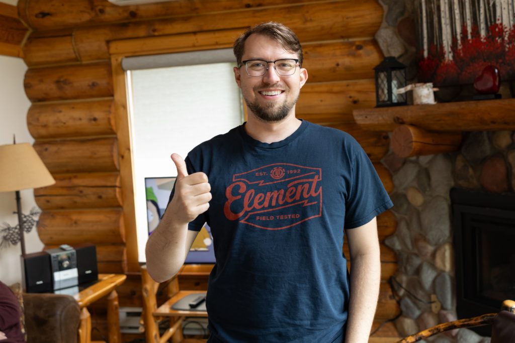 Smiling photographer Beau Petersen gives a thumbs-up in a rustic Wisconsin cabin setting, showcasing wedding