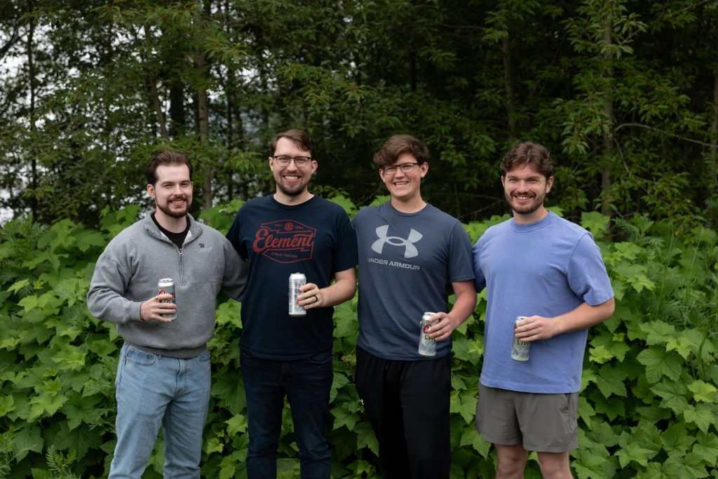Four smiling men standing outdoors in a lush green setting, likely captured by Beau Petersen