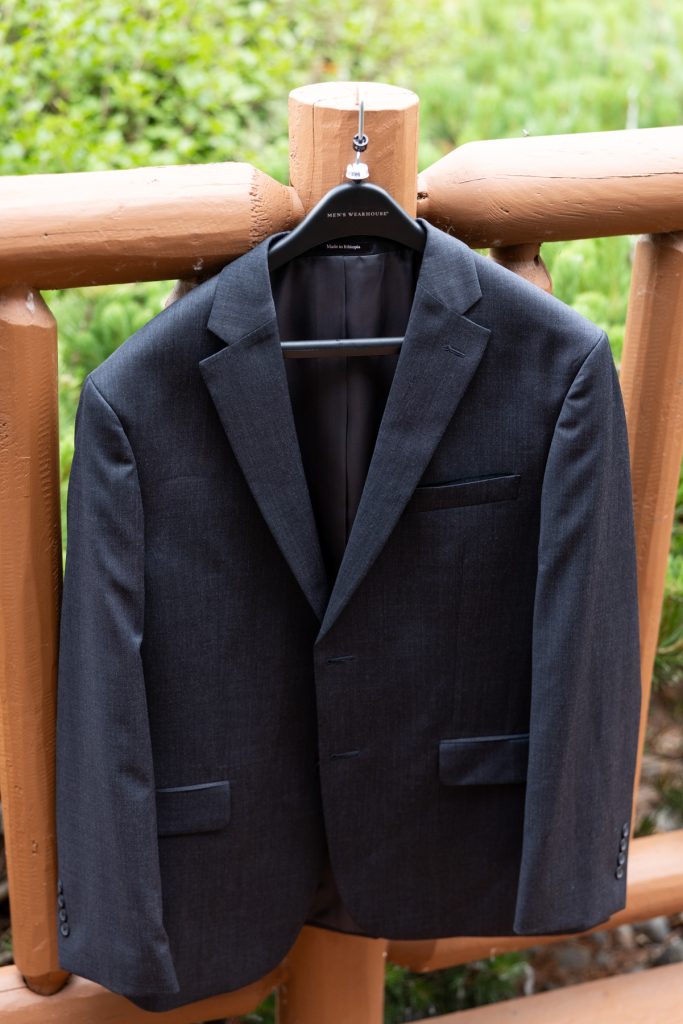 Dark gray suit jacket hanging on a hanger outdoors, showcasing wedding photography and videography services