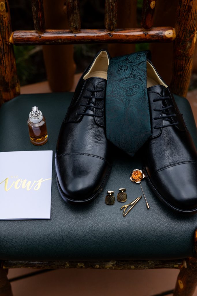 Groom's wedding details including black leather shoes, blue patterned tie, cuff links, and a "vows"