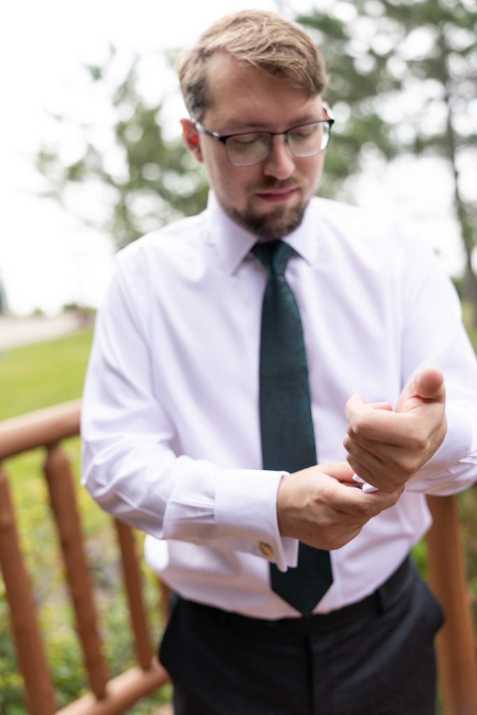 Groom in a white shirt and black tie adjusting his cufflink outdoors, captured by Beau