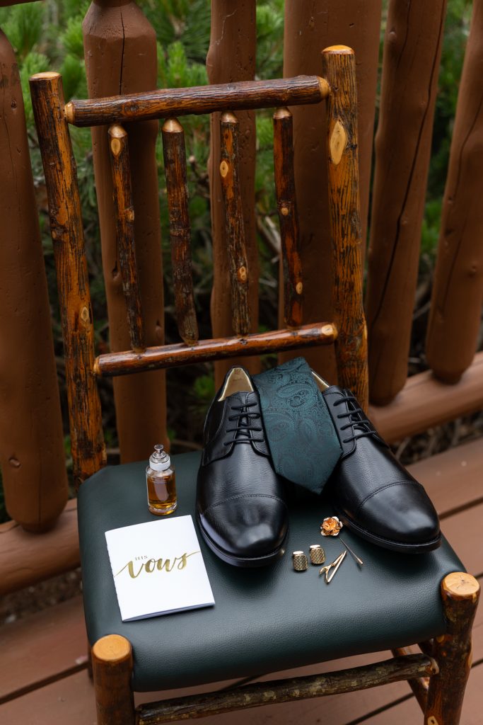 A detail shot of a groom's wedding attire arranged on a rustic chair, including black