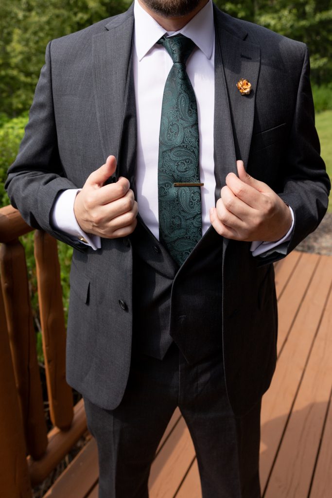 Groom in a gray suit and green tie adjusting his jacket, showcasing wedding attire