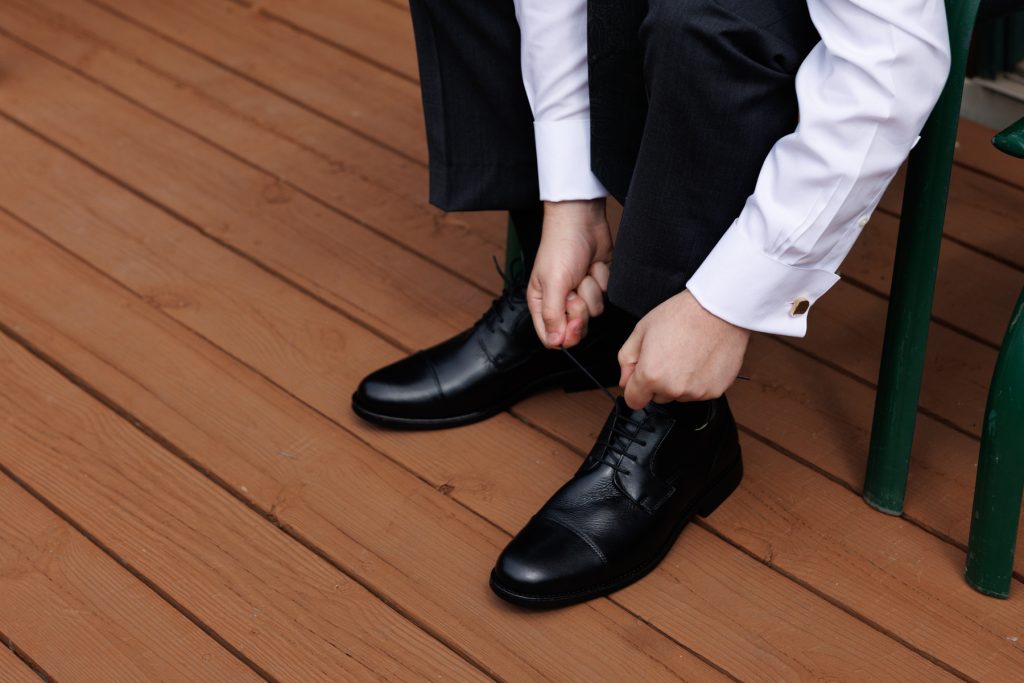Groom in a black suit and white shirt adjusting his dress shoes, capturing details