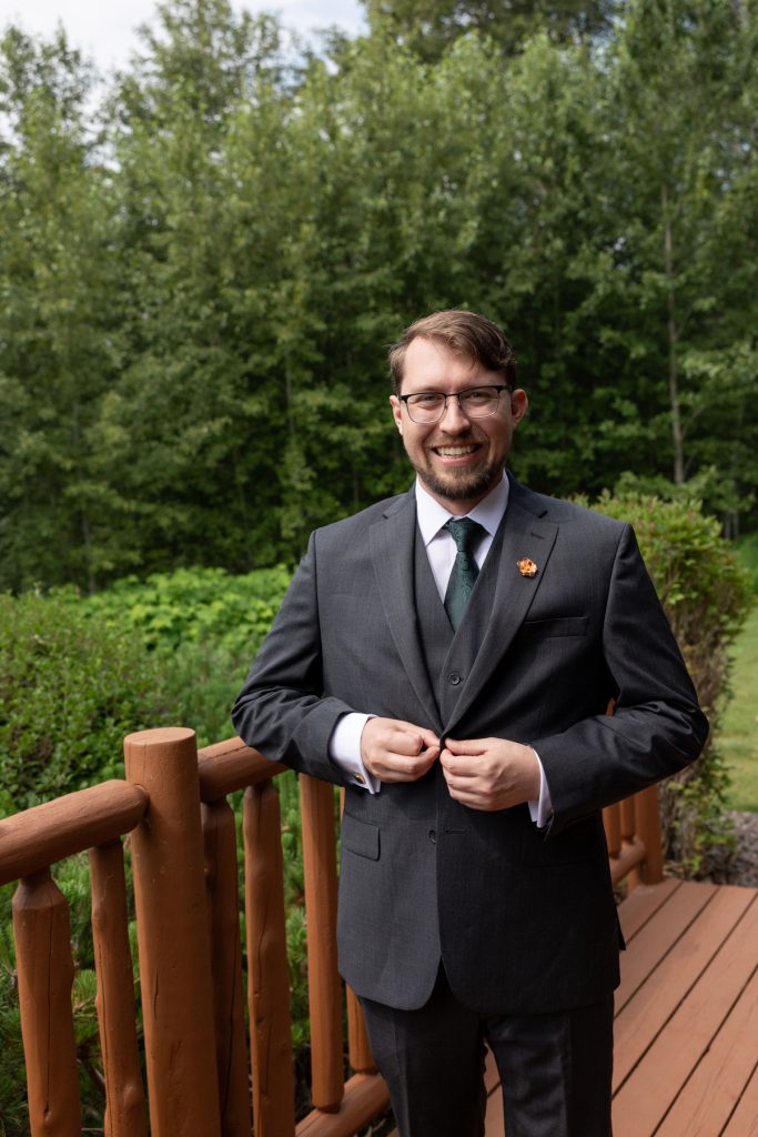 Groom in a gray suit and green tie smiles while posing outdoors, capturing a joyful
