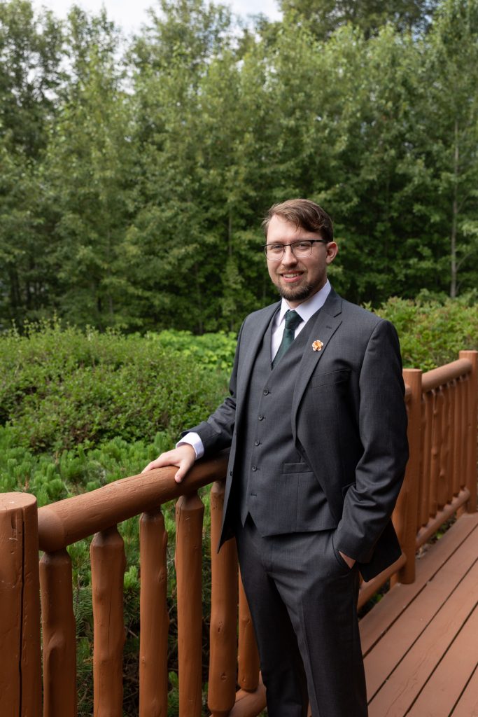 Groom in a gray suit and green tie smiles confidently while posing outdoors