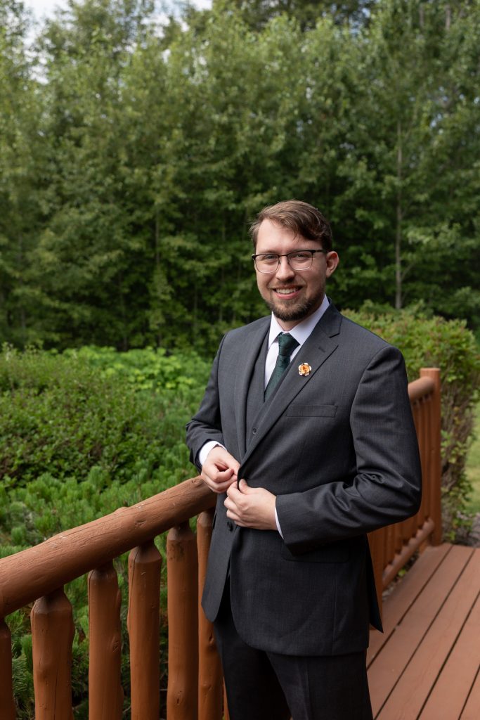 Groom in a dark gray suit and green tie smiles confidently while adjusting his jacket